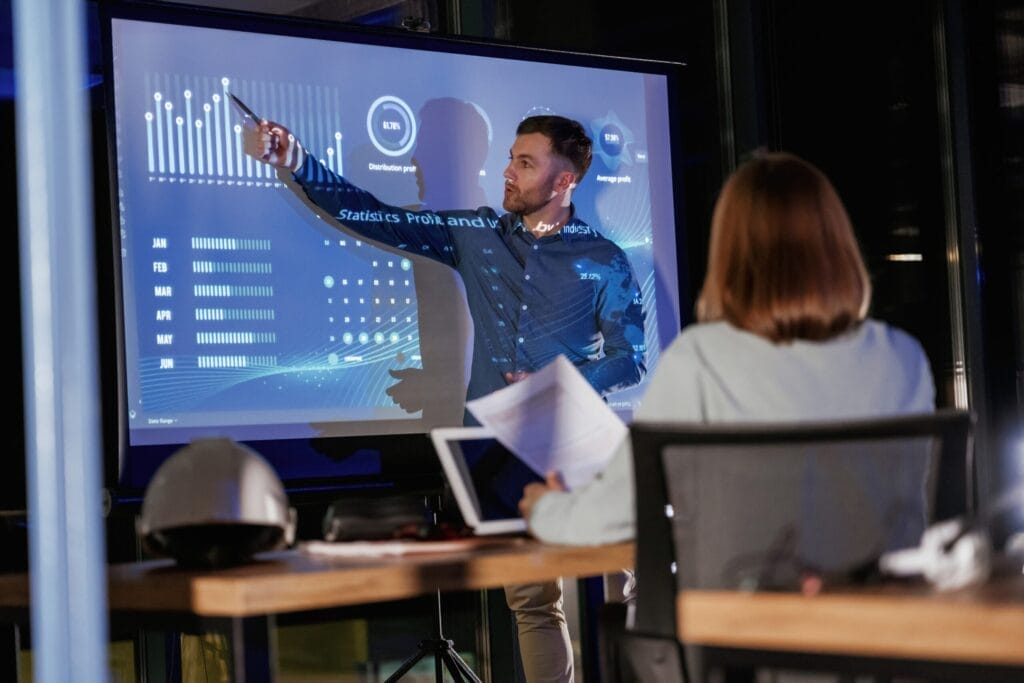 Helping to grow the company. Male business trainer is against projector with data, teaching people